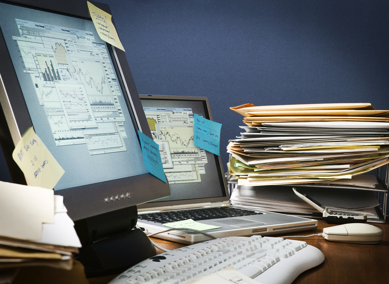 Office desk cluttered with paperwork, post-it-notes and files.